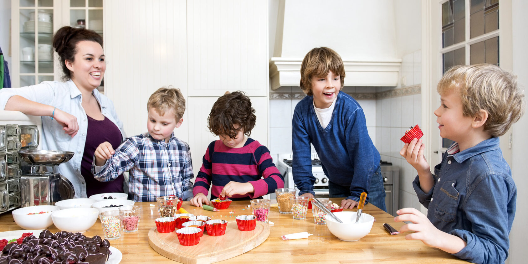 Boys and girls decorating cupcakes at a kitchen counter during a baking workshop for kids at a birthday party